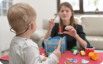 Child with hearing aid playing with an adult using toys.