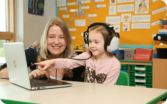 A woman and a young girl interact with a tablet in a classroom.